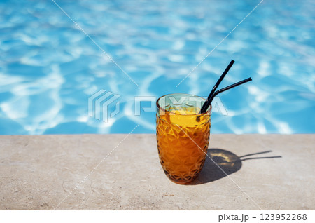 Delicious chilled fresh orange juice with straws on the side of the pool. Tasty citrus cocktail on the background of clear blue water. 123952268
