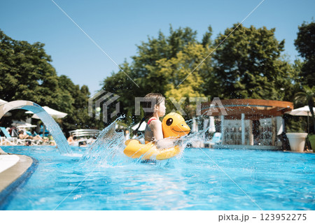 A little girl with an inflatable circle in the shape of a duck jumps into the pool. A little girl with an inflatable circle in the shape of a duck jumps into the pool. 123952275