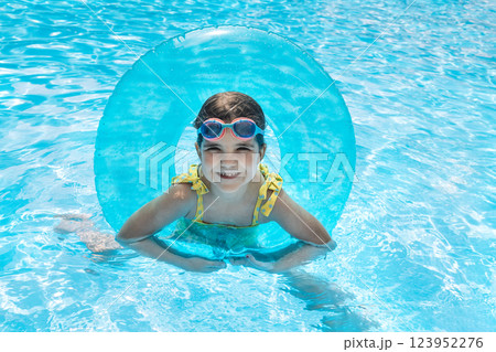 A little girl with an inflatable circle jumped into the pool. A cute kid in a swimsuit A little girl with an inflatable circle jumped into the pool. A cute kid in a swimsuit 123952276