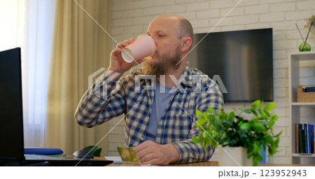 Bald man working at desk embraces comfort in home office, comfort fueling creative focus while comfort eases tension, supporting daily productivity. Remote work of man at computer 123952943