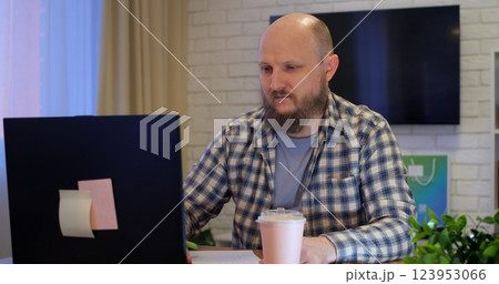 Bald man opens laptop and starts work sitting at dining table at home in room during quarantine. Work from home during quarantine or vacation. workaholic works on a day off from home 123953066