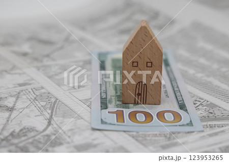 A wooden model house stands on a dollar bill against the background of a land plot scheme, 123953265