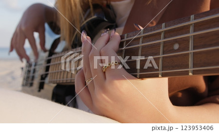 Womans Hands Playing The Bass Instrument Sitting On The Beach Womans Hands Playing The Bass Instrument Sitting On The Beach 123953406