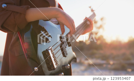 Girl Plays Bass Music Instrument On The Beach At Sunset Near Ocean Girl Plays Bass Music Instrument On The Beach At Sunset Near Ocean 123953407