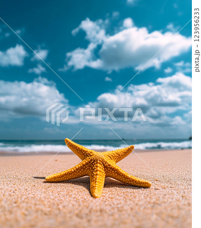 A vibrant yellow starfish with white spots rests on a sandy beach under a bright blue sky with scattered clouds and sunlight. 123956233