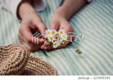 A bouquet of field white daisies plucked in a spring meadow. A young woman lying on a striped plaid with a bouquet of wildflowers. Straw female sunhat A bouquet of field white daisies plucked in a spring meadow. A young woman lying on a striped plaid with a bouquet of wildflowers. Straw female sunhat 123956395