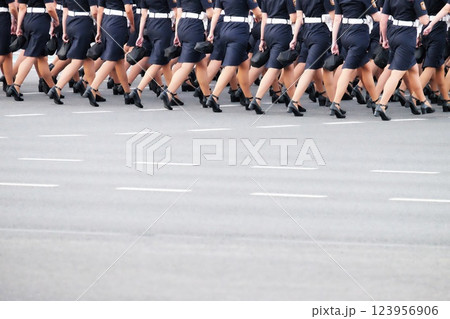A group of women in blue uniforms is marching in synchronized formation on an urban street. They wear high heels and are participating in a public ceremony with an organized display. A group of women in blue uniforms is marching in synchronized formation on an urban street. They wear high heels and are participating in a public ceremony with an organized display. 123956906
