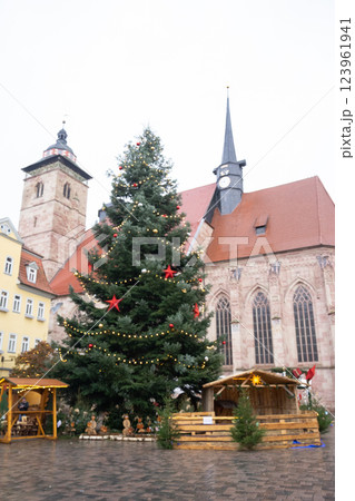 A beautifully decorated and vibrant Christmas tree stands proudly near an old historic church in a charming town center A beautifully decorated and vibrant Christmas tree stands proudly near an old historic church in a charming town center 123961941