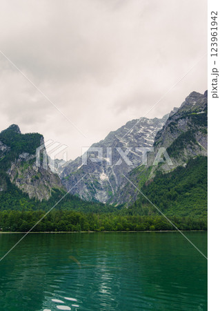 A stunning view of a lush green forest surrounded by towering mountain peaks. The serene landscape evokes a sense of peace and natural beauty, perfect for nature enthusiasts. Konigssee lake Bavaria A stunning view of a lush green forest surrounded by towering mountain peaks. The serene landscape evokes a sense of peace and natural beauty, perfect for nature enthusiasts. Konigssee lake Bavaria 123961942