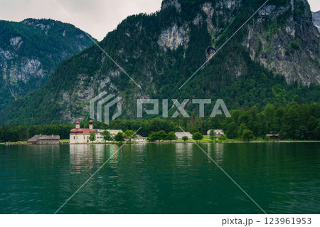 A white church with red domes stands by the tranquil waters of a lake, surrounded by lush greenery and majestic mountains on a sunny day. Konigssee lake Bavaria German Alps Berchtesgaden church by the A white church with red domes stands by the tranquil waters of a lake, surrounded by lush greenery and majestic mountains on a sunny day. Konigssee lake Bavaria German Alps Berchtesgaden church by the 123961953