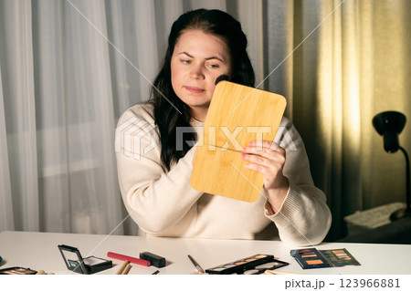 Woman doing make up looking in mirror at home. Putting on make-up with brush. Applying blush to face. Reflection in mirror. 123966881