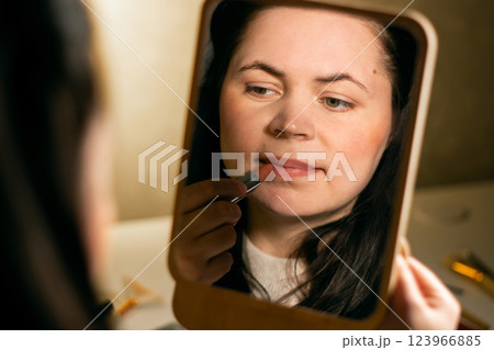 Woman looking in mirror and applying lipstick to lips. Self makeup. Preparing for event. Beauty and self-care concept. Reflection in mirror Woman looking in mirror and applying lipstick to lips. Self makeup. Preparing for event. Beauty and self-care concept. Reflection in mirror 123966885