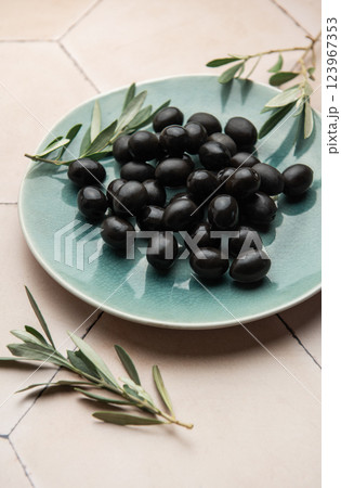 Black olives served on ceramic plate with olive branches on tiled surface Black olives served on ceramic plate with olive branches on tiled surface 123967353