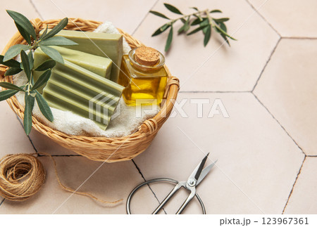 Olive soap bars, essential oil and scissors resting in wicker basket on tiled surface Olive soap bars, essential oil and scissors resting in wicker basket on tiled surface 123967361