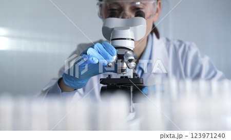 Woman scientist wearing lab coat, white protective gloves and glasses, is using microscope in modern laboratory setup, portrait view. Low key lighting photo. Science and Medicine Woman scientist wearing lab coat, white protective gloves and glasses, is using microscope in modern laboratory setup, portrait view. Low key lighting photo. Science and Medicine 123971240