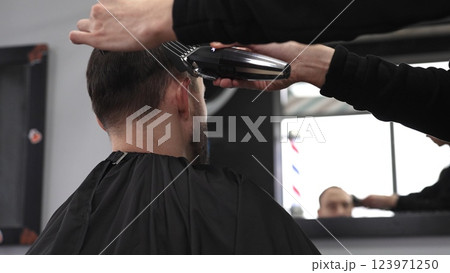Professional barber trimming male client's hair using electric razor, creating contemporary hairstyle in sleek barbershop setting, showcasing precision grooming technique 123971250