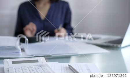 White calculator, pen and documents are lying on accountant's desk. Businesswoman wearing blue dress is working with documents on the background. Business and audit concept 123971262