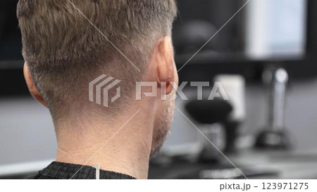 Skilled barber trimming client's hair with electric razor, demonstrating professional grooming technique in modern barbershop interior Skilled barber trimming client's hair with electric razor, demonstrating professional grooming technique in modern barbershop interior 123971275