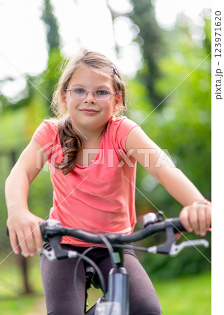 Young girl with glasses riding a bicycle outdoors in a green park, enjoying an active lifestyle and summer leisure time 123971620