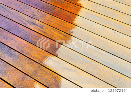 Close-up of a wooden deck being stained with a brush for protection and maintenance Close-up of a wooden deck being stained with a brush for protection and maintenance 123972194