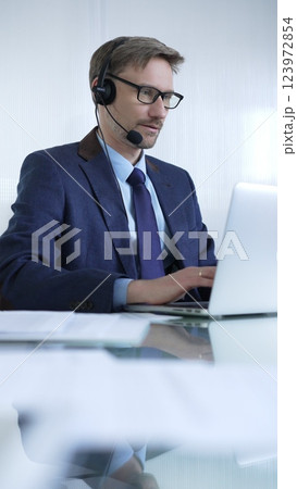 Businessman in blue suit is using a headset and laptop to offer customer service or online consultations. Business people concept Businessman in blue suit is using a headset and laptop to offer customer service or online consultations. Business people concept 123972854