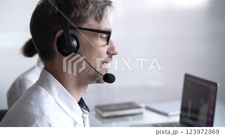 Happy smiling male call center operator in white casual shirt is assisting clients online, providing customer support and answering inquiries. Business call center operators 123972869