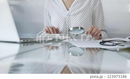 Businesswoman carefully reviewing financial reports with magnifying glass and calculator, conducting audit and analyzing data, closeup view. Taxes and audit in business 123973186