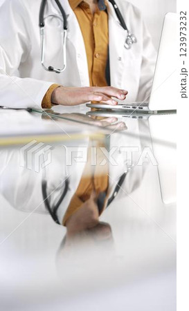 Unknown doctor man in a yellow shirt under a medical coat is using technology in medicine. Close-up of hands typing on a laptop on a glass desk in the clinic, vertical view. Health care concept Unknown doctor man in a yellow shirt under a medical coat is using technology in medicine. Close-up of hands typing on a laptop on a glass desk in the clinic, vertical view. Health care concept 123973232