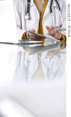 Unknown doctor woman wearing a stethoscope, yellow blouse under a lab coat, is using digital tablet in modern healthcare setting, interacting with patient data, vertical portrait. Medicine concept Unknown doctor woman wearing a stethoscope, yellow blouse under a lab coat, is using digital tablet in modern healthcare setting, interacting with patient data, vertical portrait. Medicine concept 123973240