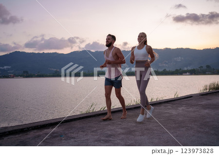 A Couple Jogging Together Alongside the Serene Lake During the Stunning Sunset Hours A Couple Jogging Together Alongside the Serene Lake During the Stunning Sunset Hours 123973828