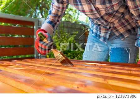 Close-up of a worker's gloved hand painting a wooden surface with a brush Close-up of a worker's gloved hand painting a wooden surface with a brush 123973900