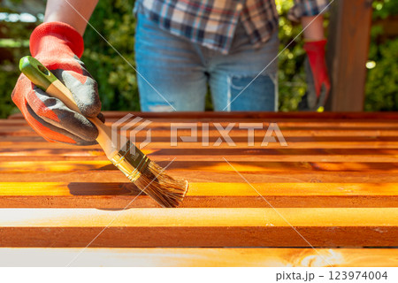 Close-up of a worker's hand applying wood stain with a paintbrush on wooden beams Close-up of a worker's hand applying wood stain with a paintbrush on wooden beams 123974004
