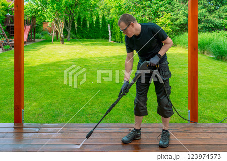 man cleaning terrace with a power washer - high water pressure cleaner on wooden terrace surface 123974573