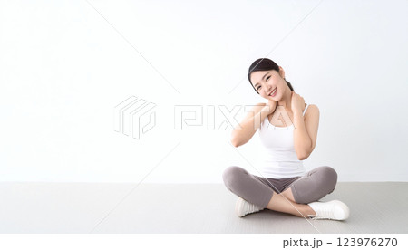 床に胡坐をかいて座っている女性。タンクトップを着て、エクササイズをしている途中の光景。 床に胡坐をかいて座っている女性。タンクトップを着て、エクササイズをしている途中の光景。 123976270