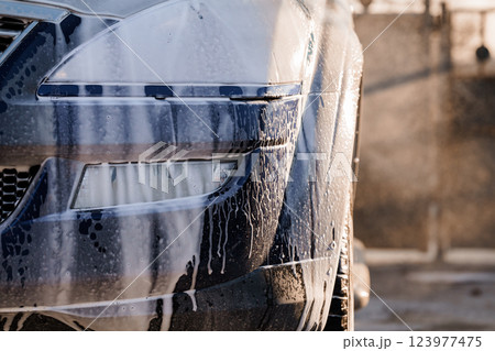 Close-up View of a Car Front Being Washed with Soap and Water Outdoors at Sunset Close-up View of a Car Front Being Washed with Soap and Water Outdoors at Sunset 123977475