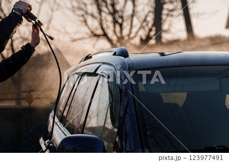 Person pressure washing black vehicle roof outdoors with water spray reflections at sunset Person pressure washing black vehicle roof outdoors with water spray reflections at sunset 123977491
