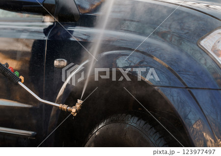 Close-up View of High-Pressure Water Spray Cleaning Dark Colored Vehicle Wheel and Fender 123977497