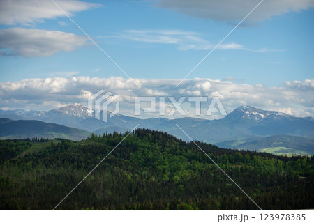 Expansive mountain landscape showcases lush greenery and distant peaks under a partly cloudy sky in early spring light 123978385