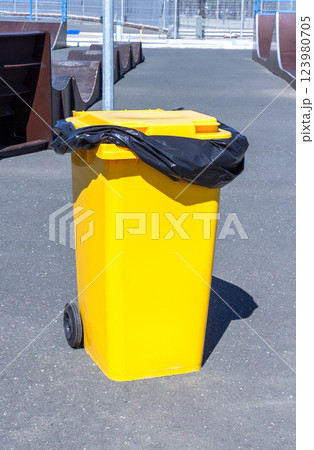 Covered yellow plastic garbage container with wheels on the street Covered yellow plastic garbage container with wheels on the street 123980705