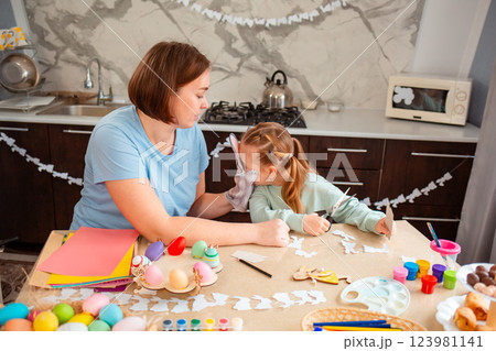Caucasian mother and happy little daughter sitting at the table and make crafts and decorations together for the Easter 123981141