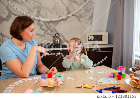 Smiling mother and cute little girl play together with rabbit glove, sitting at Easter table. Spring holiday 123981158