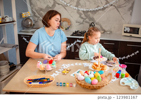 Wide shot of Caucasian mother and her child sitting at the festive table for Easter and prepares decorations 123981167