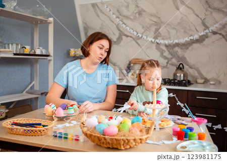 Wide shot of mother and her child sitting at the festive table for Easter and prepares decorations 123981175