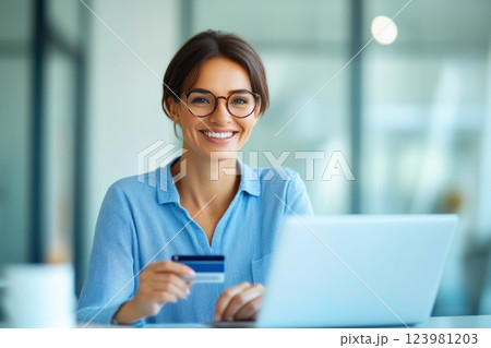 Happy woman using credit card while working on laptop in office 123981203