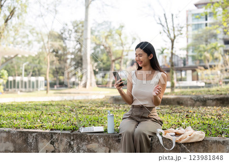Sustainable lifestyle. Woman engaging with smartphone outdoors in a park setting. 123981848