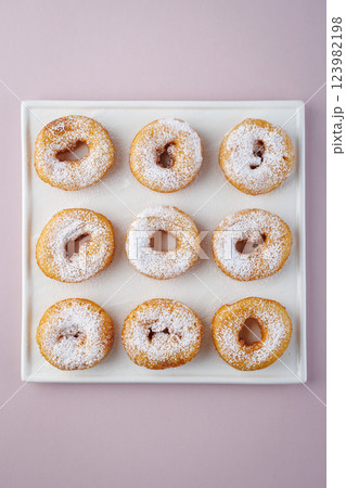 Donuts with powdered sugar on a light plate and a delicate purple background. Top view Donuts with powdered sugar on a light plate and a delicate purple background. Top view 123982198