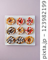 donuts with powdered sugar and various toppings on a white plate on a pale purple background. Top view . Copy space 123982199