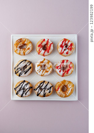 donuts with powdered sugar and various toppings on a white plate on a pale purple background. Top view . Copy space donuts with powdered sugar and various toppings on a white plate on a pale purple background. Top view . Copy space 123982199
