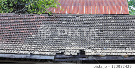 Broken tile roof, weathered gray tiles on roof of old building, construction and architecture. 123982429