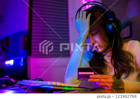 Young Asian woman gamer wearing headphones unset suffer of overspending money from card account after pay game online, problem using credit card, playing gaming with money 123982769